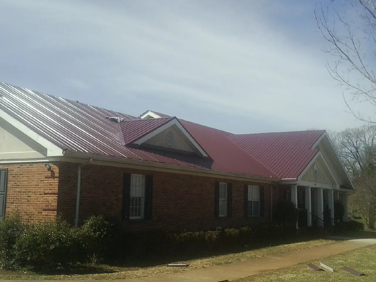 Red metal roof with gabled entries on a long brick building, from a Hail Damage Roof Repair job in Ramseur