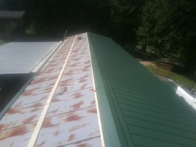 Old rusted panels beside newly installed green metal roofing — Wind Damage Roof Repair by Roofing Brothers in Ramseur