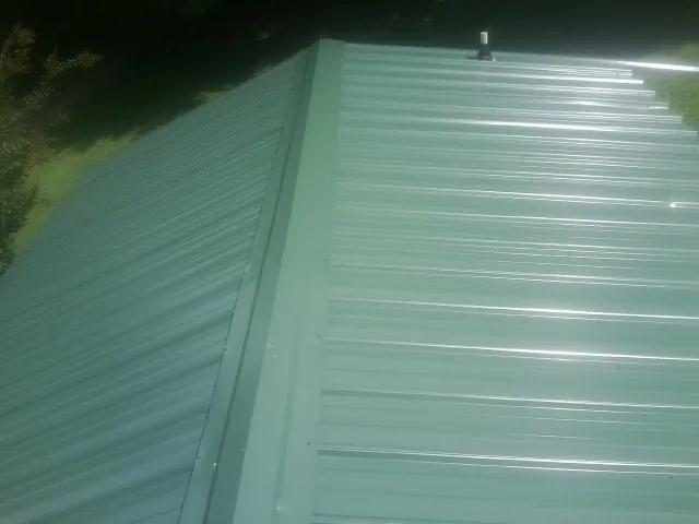 New green metal panels meeting at the ridge of a roof — Flat Roof Repair work by our crew in Ramseur
