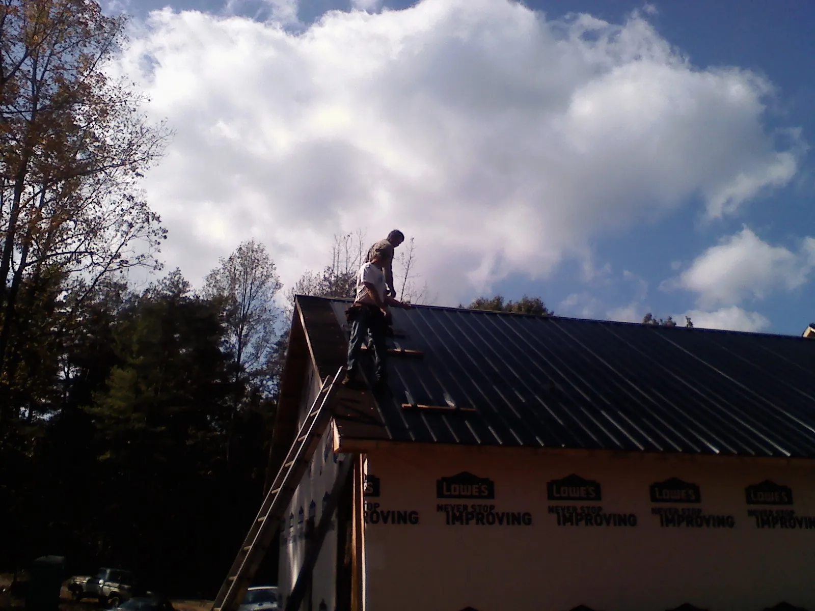Roofer fastening dark metal panels high against a cloudy sky, from a Roof Inspection job in Ramseur